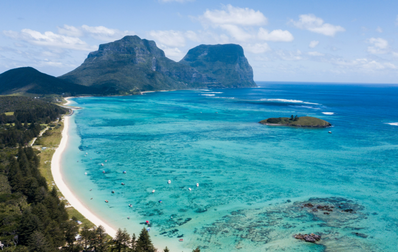 Lord Howe Island, with tall forest-covered mountains, white sandy beaches, and a clear, blue offshore reef