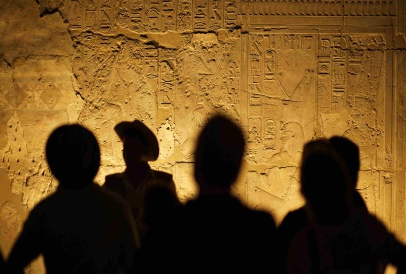 Four human silhouettes on an interior wall of an Egyptian temple covered in hieroglyphics