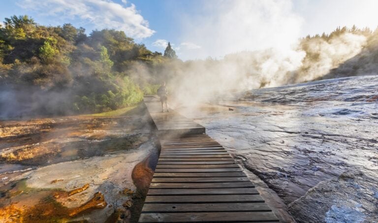 Tourist on a wooden boardwalk surrounded by steam from geothermal activity, Lake Taupo, New Zealand