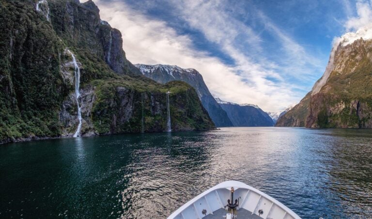 The prow of a boat cruises past waterfalls along Milford Sound, New Zealand