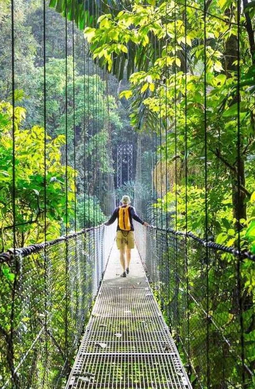 A man walking across a hanging bridge through the rainforest in Arenal, Costa Rica