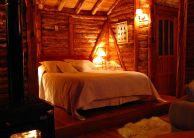 A bedroom in a log cabin lit up by lamps at Mallín Colorado, Chile