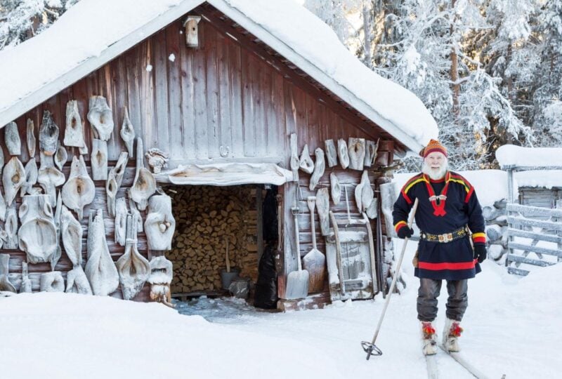 A Sami man stands on skis outside a snow covered lodge in Finnish Lapland