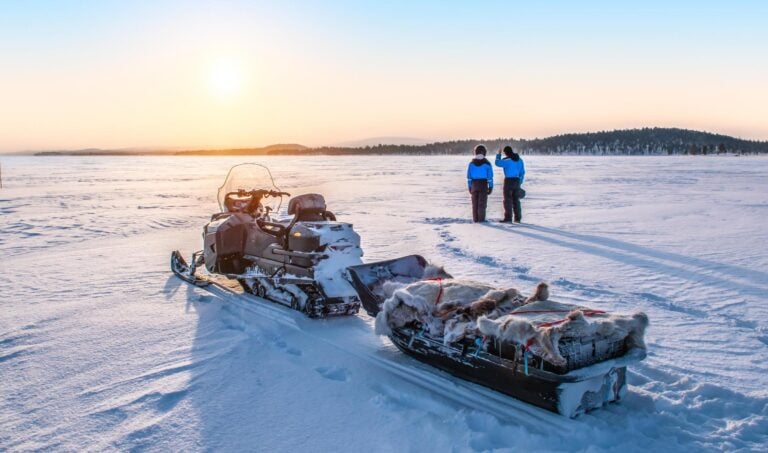 Two people watching sunset with a snowmobile in Finnish Lapland