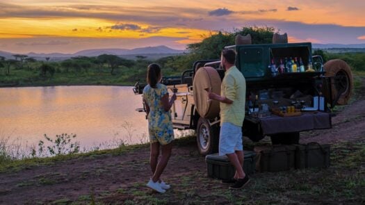 A couple having a sunset drink from a safari jeep