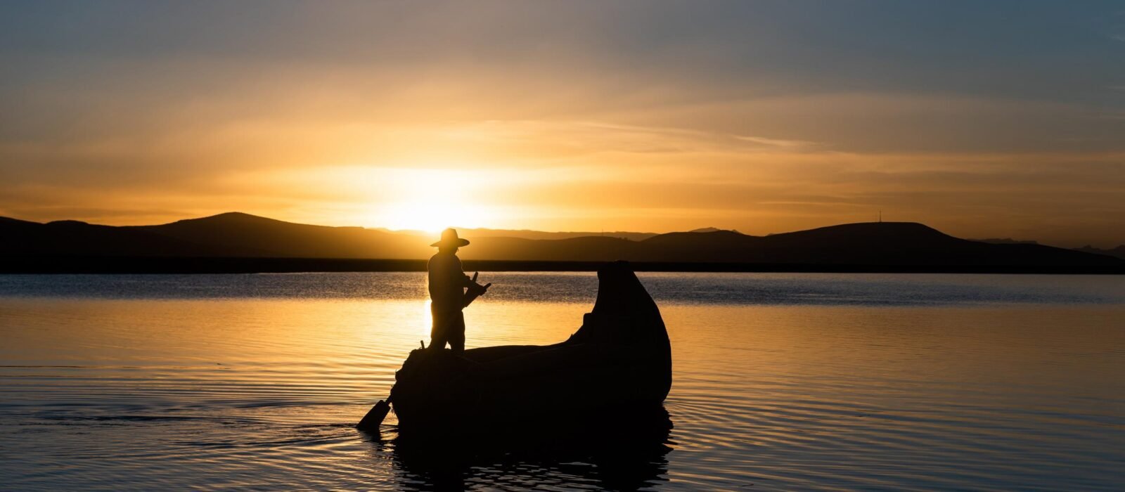 Man in traditional costume sailing in a traditional boat on lake titicaca at sunset puno peru