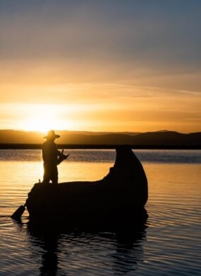 Man in traditional costume sailing in a traditional boat on lake titicaca at sunset puno peru