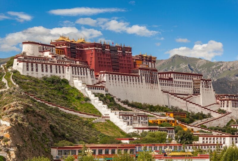 The Potala Palace in Lhasa, Tibet, against a backdrop of blue skies and mountains.