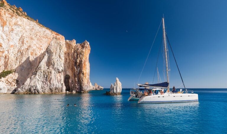 A boat anchored next to a rocky outcrop in Milos, Greece