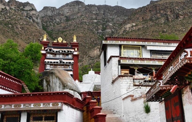 Tibetan monastery with ornate architecture against rocky mountains.