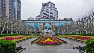 Urban park with colorful flower beds, a fountain, leafless trees, and a classical building background.